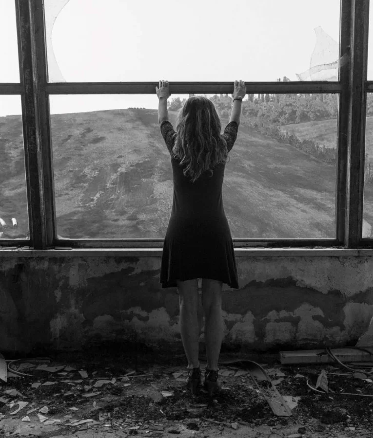 Ασπρόμαυρη φωτογραφία γυναίκας που στέκεται μπροστά από μεγάλο παράθυρο κοιτάζοντας το τοπίο έξω, youngpeople.gr