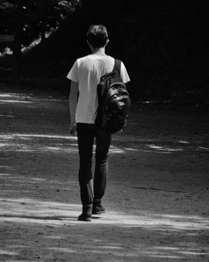 Ασπρόμαυρη φωτογραφία ενός νεαρού άνδρα με σακίδιο πλάτης που περπατά μόνος σε μονοπάτι, youngpeople.gr